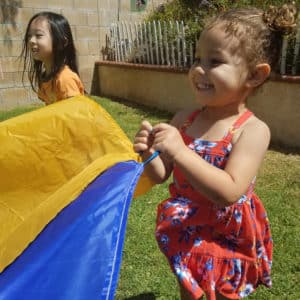 little preschool girl playing outdoors with giant colorful parachute