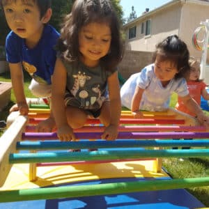 little preschool aged kids climbing on a colorful rainbow pikler triangle